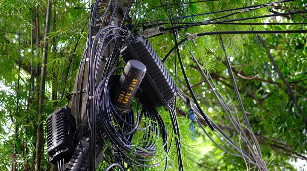 Poste de comunicaciones tecnológicas con cables y equipos rodeados de vegetación.