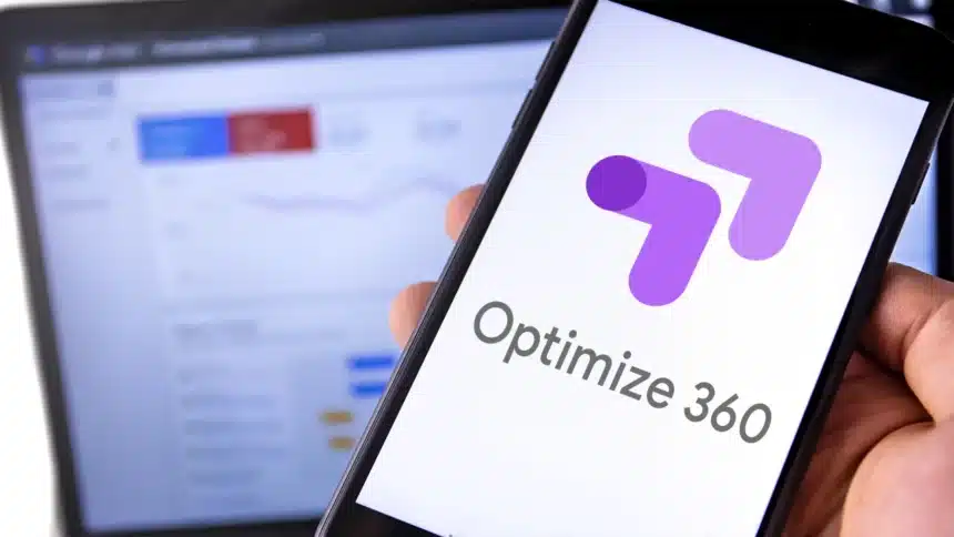 Usuario sosteniendo un teléfono móvil con pantalla que muestra el logo de Google Optimize 360. En segundo plano, una laptop muestra estadísticas difusas de un sitio web en Google.